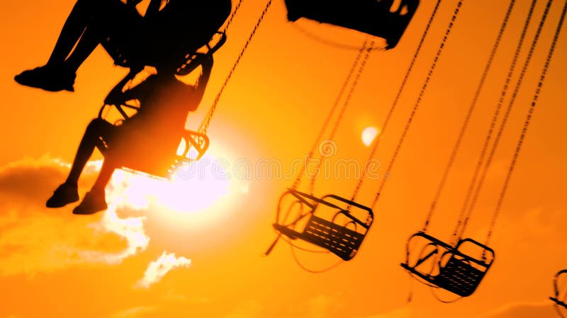 Siluetas de personas montadas sobre el carrusel encadenado contra el cielo cálido al atardecer