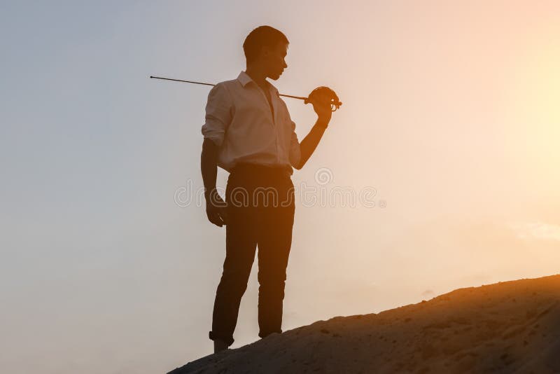 Siluetas de un hombre con una espada contra el cielo de la puesta de sol. imagen de archivo