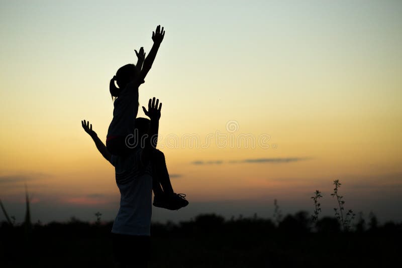 Siluetas del padre y de la hija en sus hombros con las manos encima del divertirse, contra el cielo de la puesta del sol imagenes de archivo Siluetas del padre y de la hija en sus hombros con las manos encima del divertirse, contra el cielo de la puesta del sol imagenes de archivo