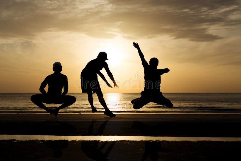 Siluetee al grupo de amigos que saltan en la playa en puesta del sol imagenes de archivo Siluetee al grupo de amigos que saltan en la playa en puesta del sol imagenes de archivo