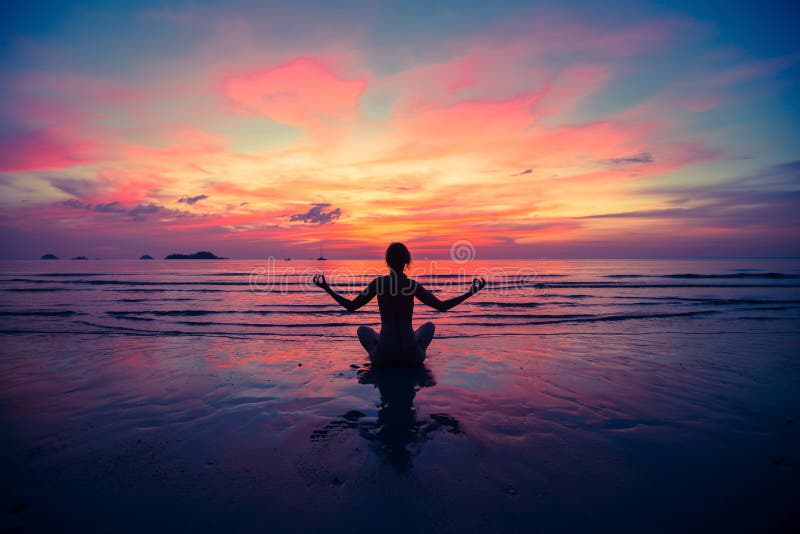 Siluetee la yoga practicante de la mujer joven en la playa en la puesta del sol Relájese imagen de archivo Siluetee la yoga practicante de la mujer joven en la playa en la puesta del sol Relájese imagen de archivo