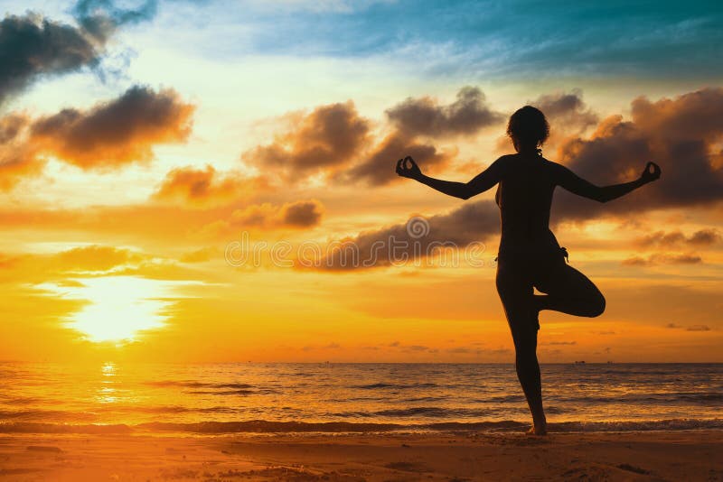 Siluetee la yoga practicante de la mujer joven en la playa en la puesta del sol Relájese fotografía de archivo Siluetee la yoga practicante de la mujer joven en la playa en la puesta del sol Relájese fotografía de archivo
