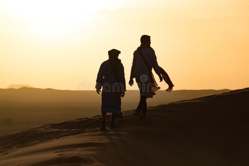 Siluetta del berbero e del cammello al tramonto rosso sanguinoso, Merzouga nel Marocco, Sahara Desert, Nord Africa fotografia stock Siluetta del berbero e del cammello al tramonto rosso sanguinoso, Merzouga nel Marocco, Sahara Desert, Nord Africa fotografia stock