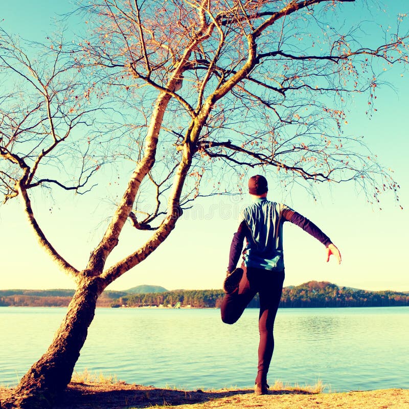 Siluetta dell'uomo attivo di sport in leggins correnti e della camicia blu all'albero di betulla sulla spiaggia Acqua calma, isol fotografia stock Siluetta dell'uomo attivo di sport in leggins correnti e della camicia blu all'albero di betulla sulla spiaggia Acqua calma, isol fotografia stock