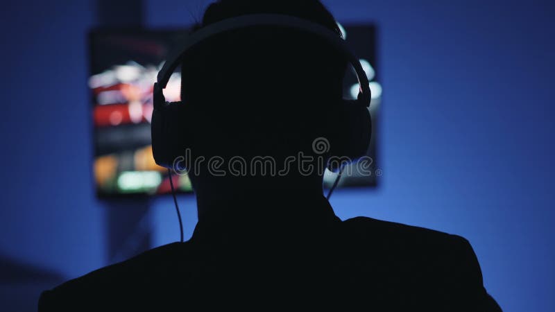 Siluetta dell'uomo in cuffie che giocano video gioco interessante a casa alla notte
