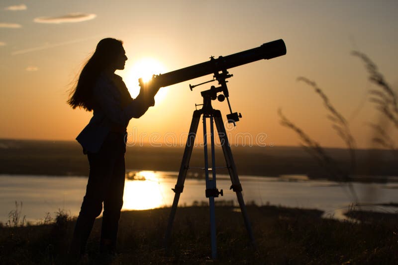 Siluetta della giovane donna che osserva vista tramite il telescopio il tramonto di estate immagini stock Siluetta della giovane donna che osserva vista tramite il telescopio il tramonto di estate immagini stock