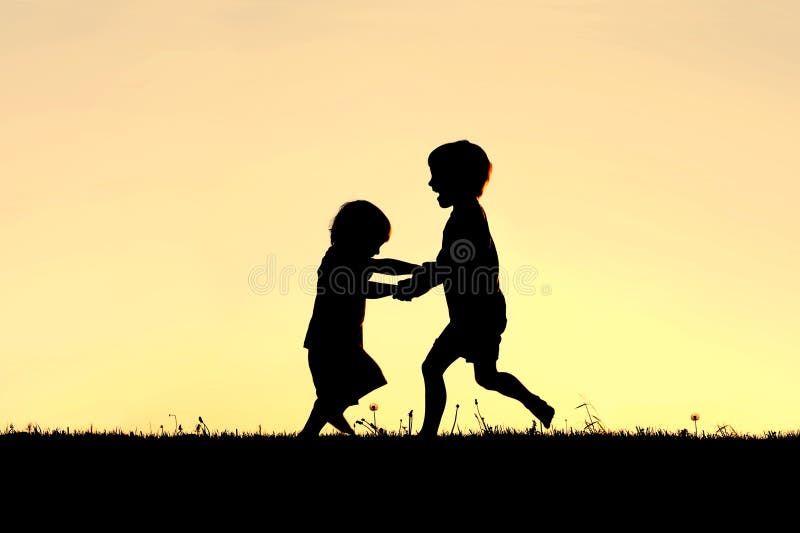 Siluetta di piccoli bambini felici che ballano al tramonto immagine stock