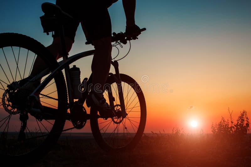 Siluetta di un motociclista e di una bicicletta sul fondo del cielo fotografie stock libere da diritti Siluetta di un motociclista e di una bicicletta sul fondo del cielo fotografie stock libere da diritti