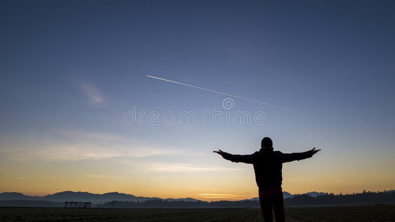 Siluetta di un uomo che sta con il suo di nuovo alla macchina fotografica in un immagine stock Siluetta di un uomo che sta con il suo di nuovo alla macchina fotografica in un immagine stock