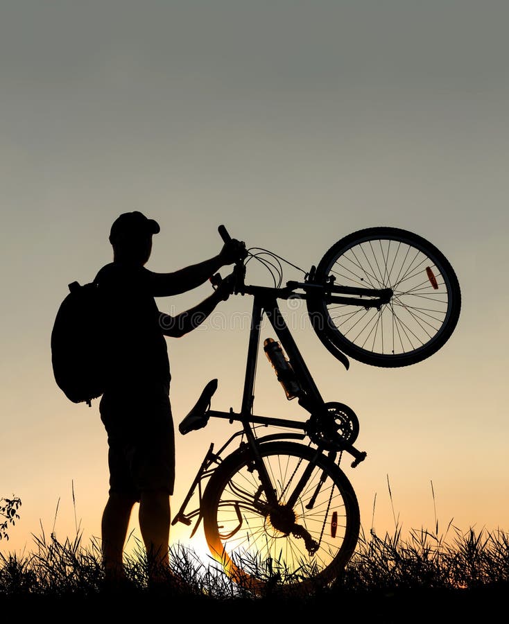 Siluetta di un uomo del ciclista con uno zaino al tramonto con la bicicletta fotografie stock Siluetta di un uomo del ciclista con uno zaino al tramonto con la bicicletta fotografie stock