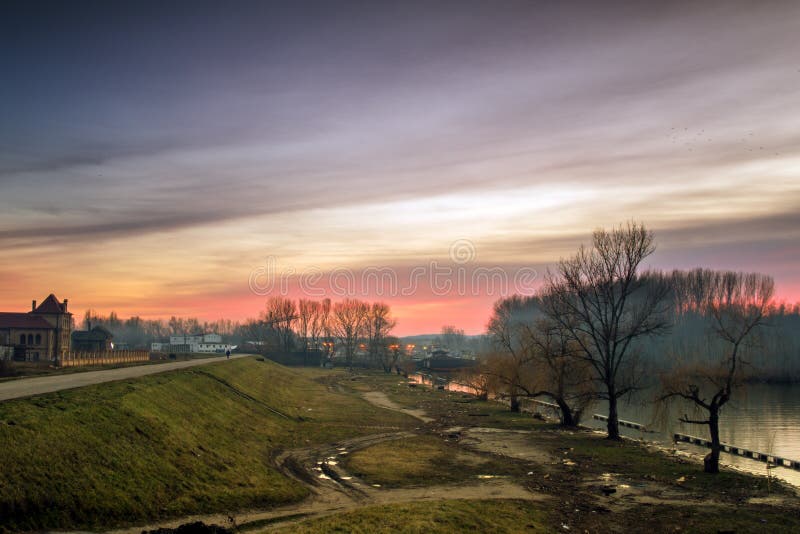 Siluetta di un uomo solo nella distanza nel tramonto alla sponda del fiume fotografie stock libere da diritti Siluetta di un uomo solo nella distanza nel tramonto alla sponda del fiume fotografie stock libere da diritti