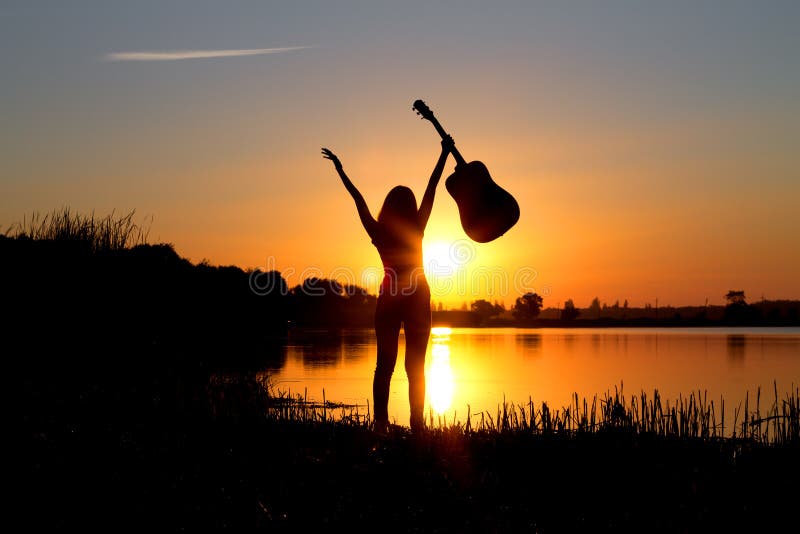 Siluetta di una ragazza felice con una chitarra sulla natura fotografie stock libere da diritti Siluetta di una ragazza felice con una chitarra sulla natura fotografie stock libere da diritti