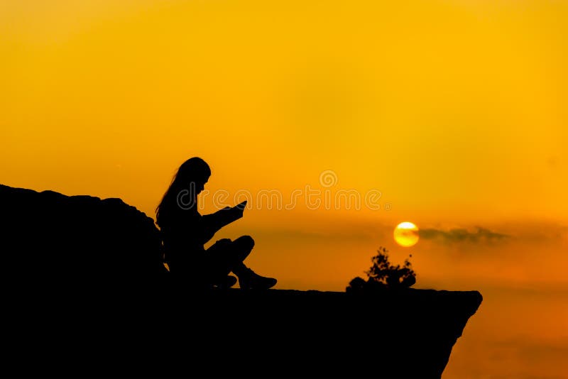 Siluetta, ragazza che legge un libro al tramonto fotografia stock
