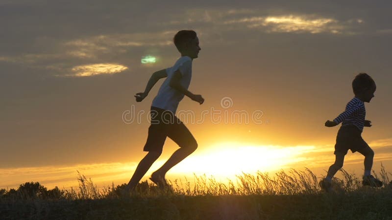 Siluette dei bambini correnti in un campo al tramonto