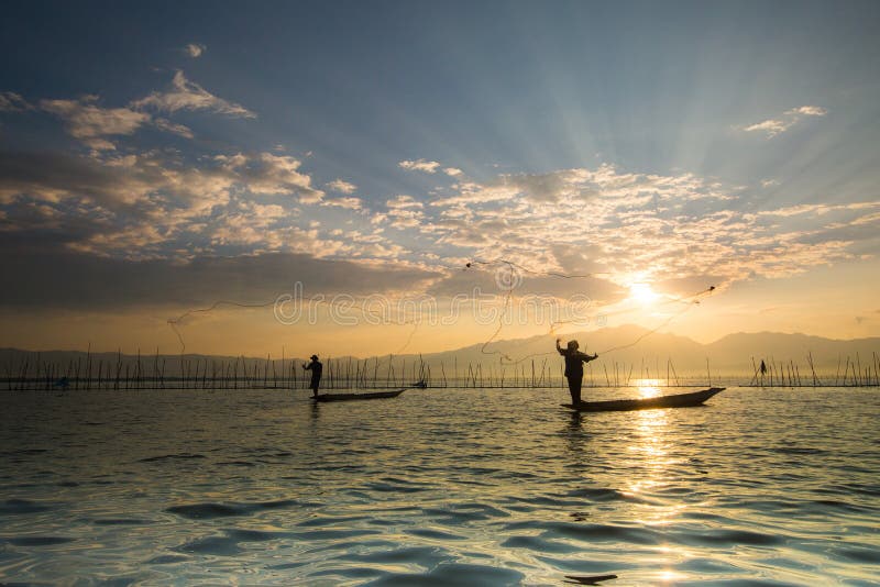 Siluette dei pescatori tradizionali che gettano rete da pesca du fotografia stock libera da diritti Siluette dei pescatori tradizionali che gettano rete da pesca du fotografia stock libera da diritti