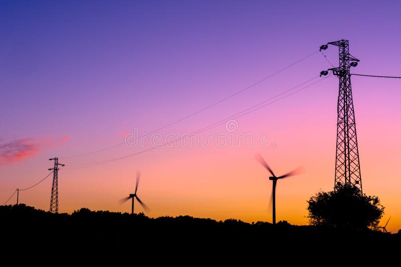 Siluette delle turbine di vento e dei piloni di elettricità