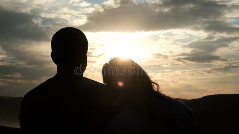 Siluette di una coppia di giovani al tramonto Una donna mette delicatamente la sua testa sulla spalla del suo uomo