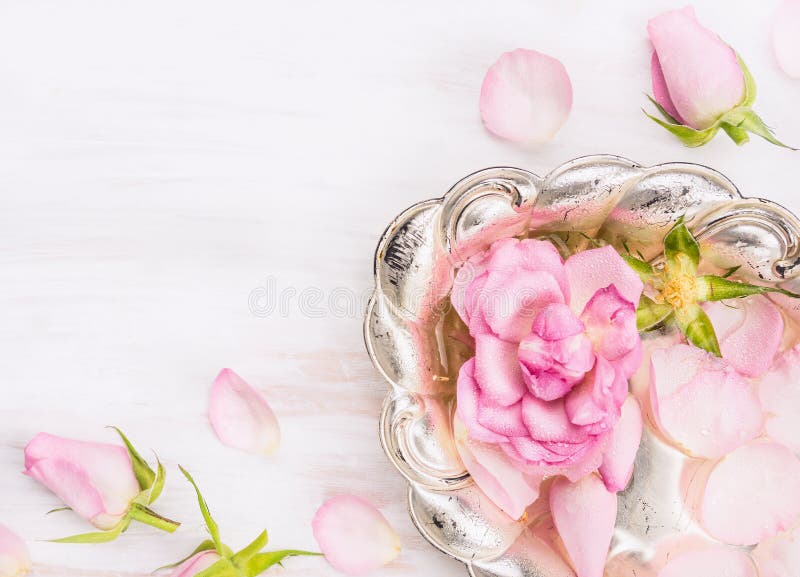 Silver bowl with roses and water on white wooden background