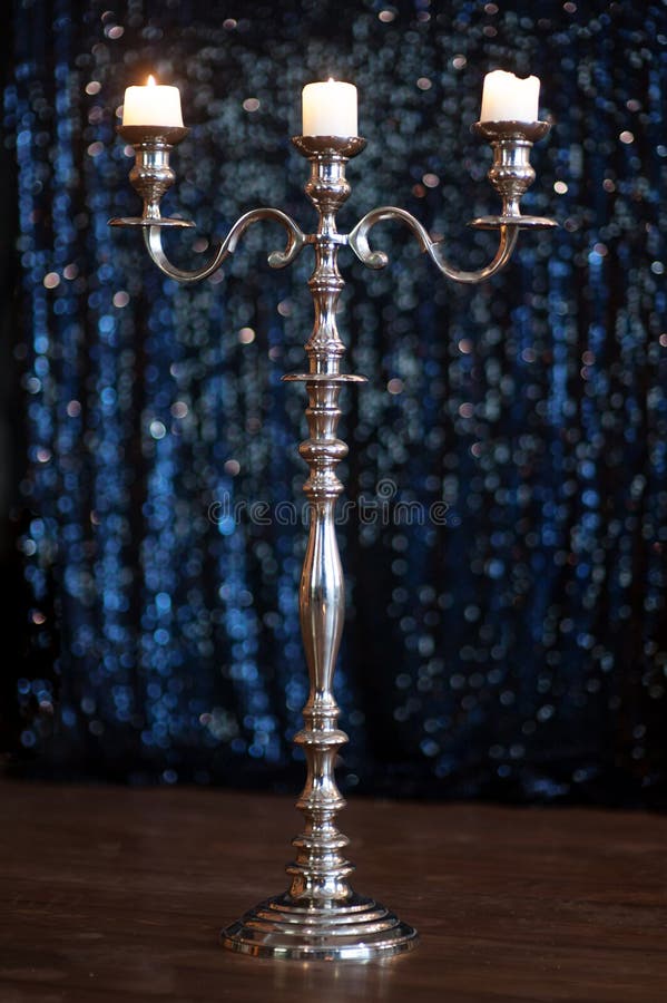Silver candlestick with three burning white candles on dark background