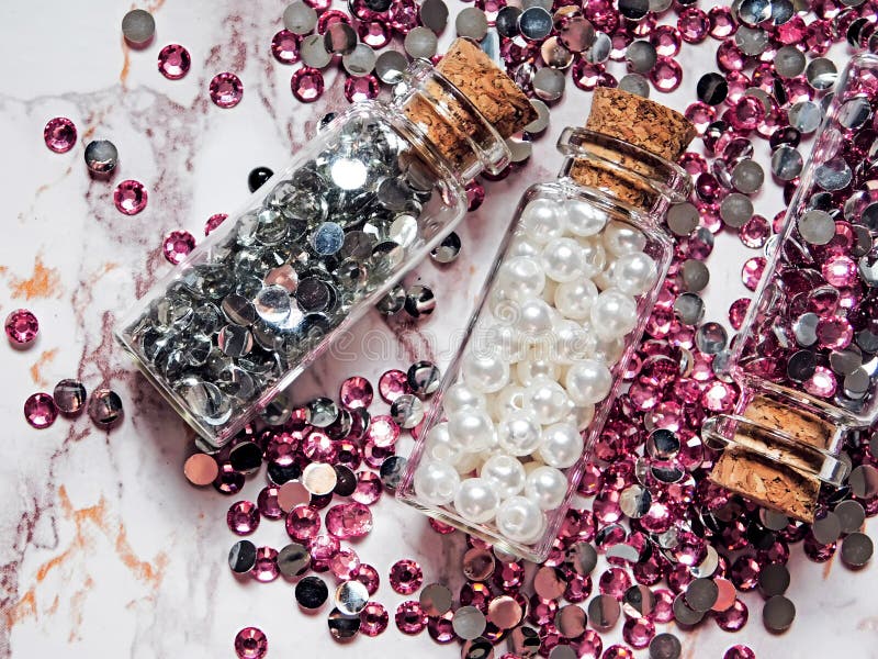Silver and pink rhinestones and white pearls in glass jars with wooden lids on a marble background stock photos Silver and pink rhinestones and white pearls in glass jars with wooden lids on a marble background stock photos