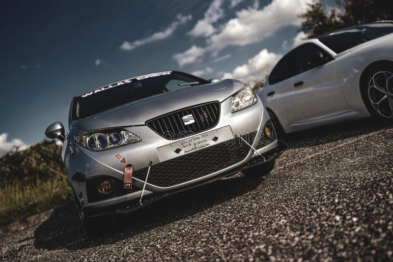 Milan, italy 20 september 2025: silver seat ibiza custom car with performance modifications and a red tow strap, parked on gravel with another vehicle under a blue sky.