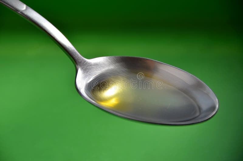 Silver spoon with olive oil on a green background close up.