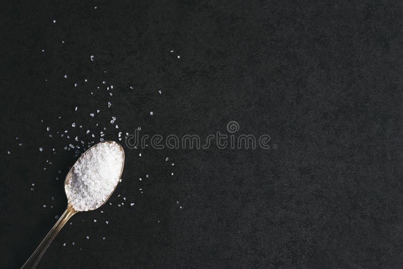 Silver spoon with salt on dark gray background