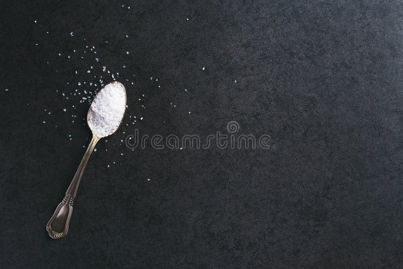 Silver spoon with salt on dark gray background