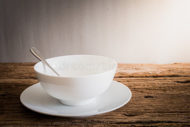 Silver spoon in white bowl and white plate on wooden tabletop