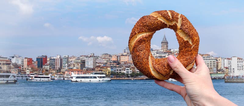 Simit turco tradicional del panecillo en una mano femenina en el fondo del panorama de Estambul y de la torre de Galata fotos de archivo libres de regalías Simit turco tradicional del panecillo en una mano femenina en el fondo del panorama de Estambul y de la torre de Galata fotos de archivo libres de regalías