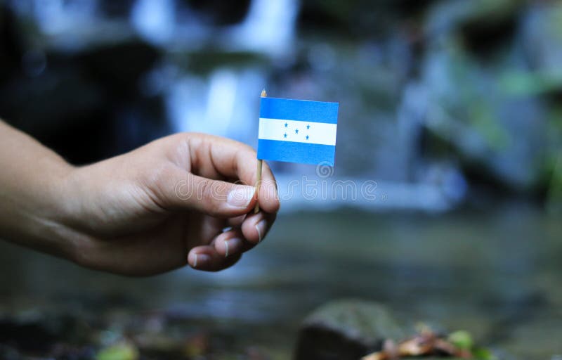 Simple and beautiful flag of Honduras on wooden stick and water and stream in background. Colour man holds state symbol and waves