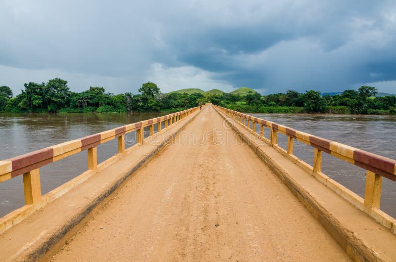 Simple dirt road bridge over tropical river with dramatic clouds in Republic of Congo, Africa