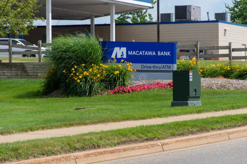 Sinal azul do banco de Macatawa com movimentação completamente, atm e flores na grama verde e no céu azul imagens de stock Sinal azul do banco de Macatawa com movimentação completamente, atm e flores na grama verde e no céu azul imagens de stock