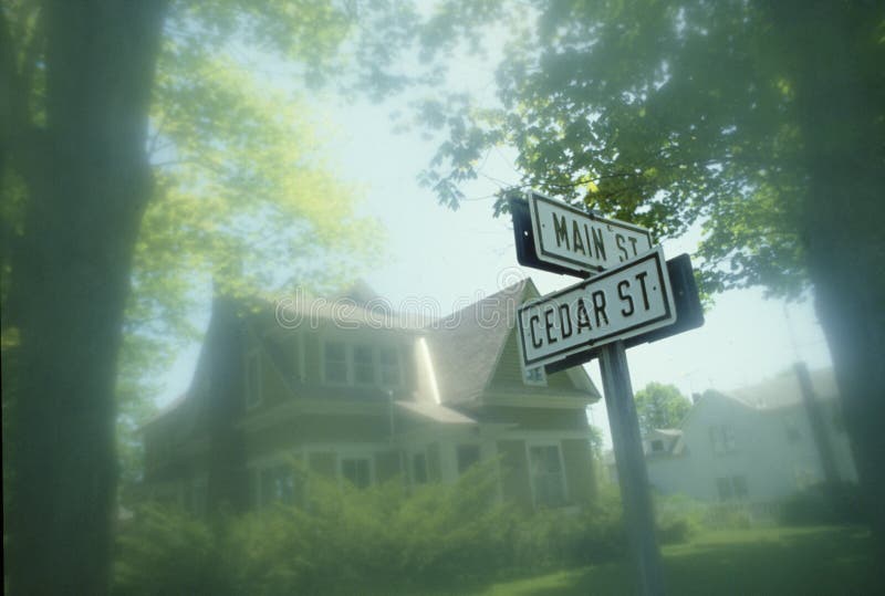 Sinal de rua no canto do cano principal e do cedro com a casa vitoriano no fundo, Michigan imagens de stock Sinal de rua no canto do cano principal e do cedro com a casa vitoriano no fundo, Michigan imagens de stock