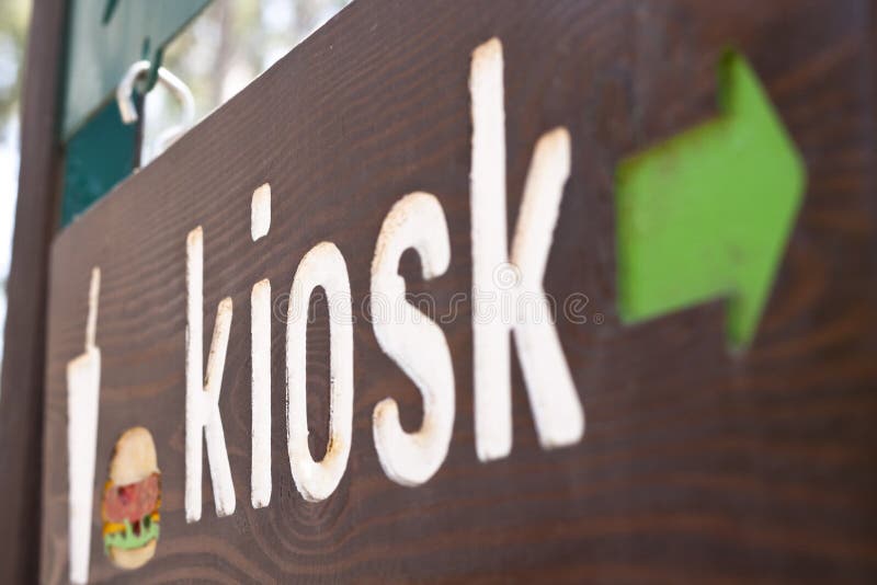 A wood sign with a green arrow with a hamburger and kiosk. A wood sign with a green arrow with a hamburger and kiosk