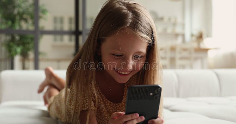 Sorridente menina deitada no sofá confortável, gostando de jogar