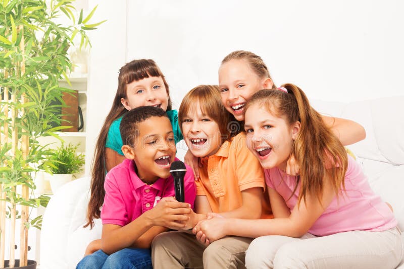 Close-up shoot of group of five happy little kids, boys and girls, singing together sitting on the coach in living room at home. Close-up shoot of group of five happy little kids, boys and girls, singing together sitting on the coach in living room at home