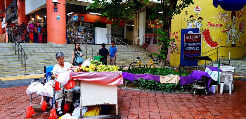 Singapour, Singapour 29 juin 2018 : Dame âgée vendant le fruit sur le marché de nourriture de rue avec les personnes brouillées e photo stock Singapour, Singapour 29 juin 2018 : Dame âgée vendant le fruit sur le marché de nourriture de rue avec les personnes brouillées e photo stock