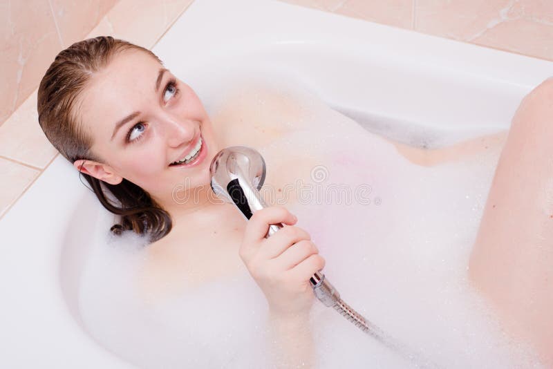 Happy smiling blond beautiful young woman relaxing taking bath singing using shower as microphone and looking up at copy space portrait picture. Happy smiling blond beautiful young woman relaxing taking bath singing using shower as microphone and looking up at copy space portrait picture
