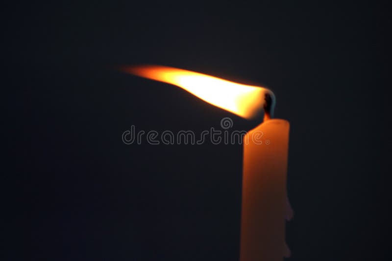 Single Candle Burning Flame Blowing Against a Black Background Stock