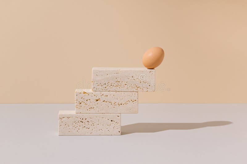 Single egg leaning on the edge of a travertine marble blocks steps on a beige and gray background. stock image