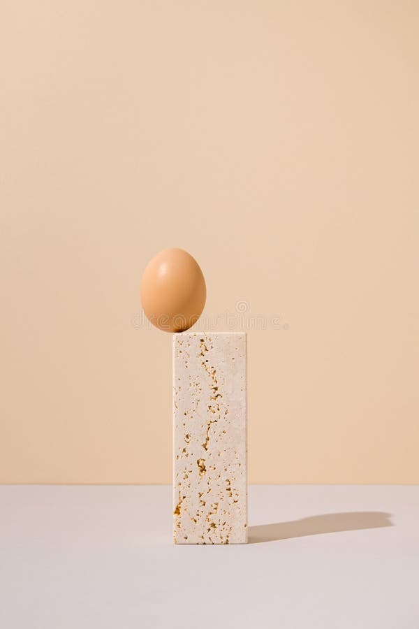 Single egg standing on a travertine marble block on a beige and gray background. 2021 Easter unique still life arrangement. royalty free stock photography