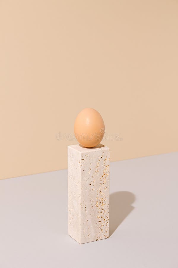 Single egg standing on a travertine marble block on a beige and gray background. 2021 Easter unique still life composition. royalty free stock photography