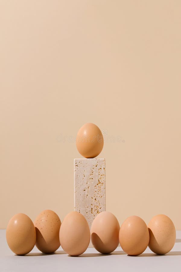 Single egg standing on a travertine marble block stage surrounded by group of eggs on a beige and gray background. stock photos