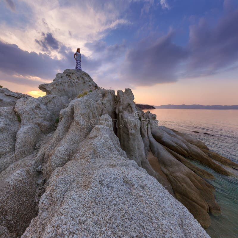 Single girl watching sunset high up on cliff by sea