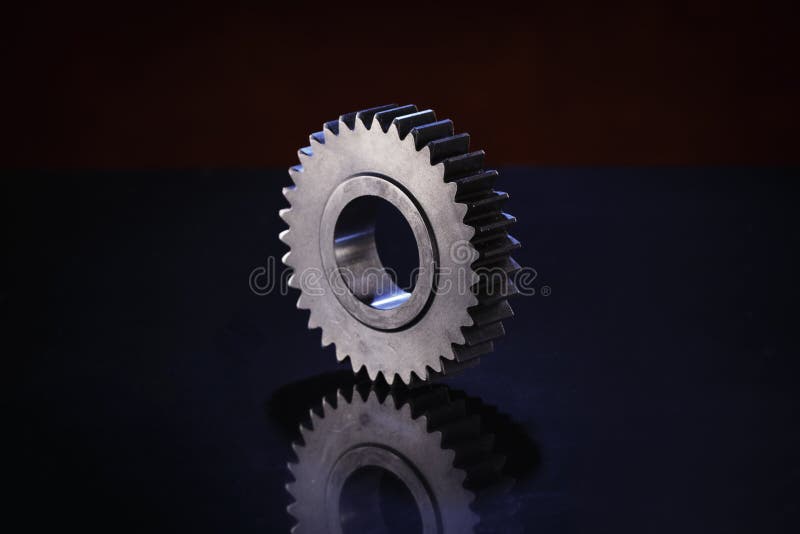 A single, metallic gear rests on a dark, reflective surface royalty free stock photo