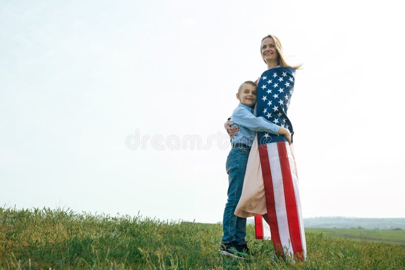 Single mother with son on independence day of USA. Woman and her child walk with the USA flag on the ocean coast