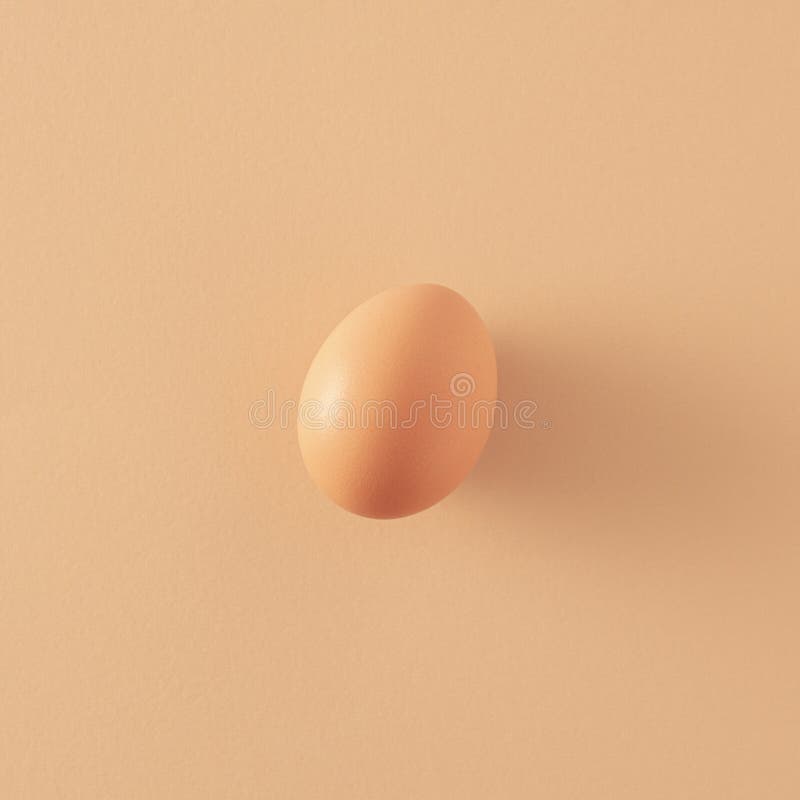 Single natural egg standing on a pastel beige paper background. 2021 Easter unique still life layout. Minimal retro creative idea. stock photography