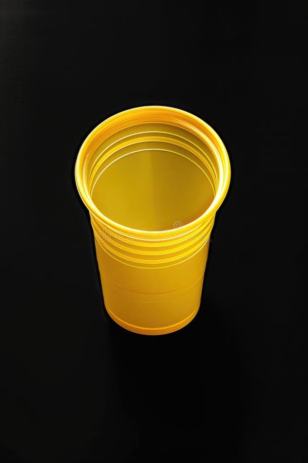 A single yellow plastic cup sits on a black surface royalty free stock images