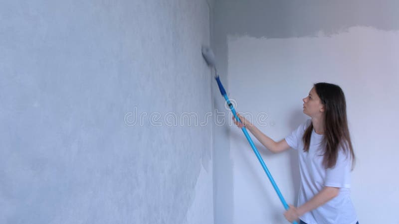 Single young girl painter is painting wall in gray using paint rollers in flat.